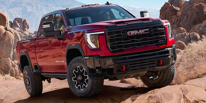 Red Sierra 3500 truck standing on rocks in a desert landscape under clear skies