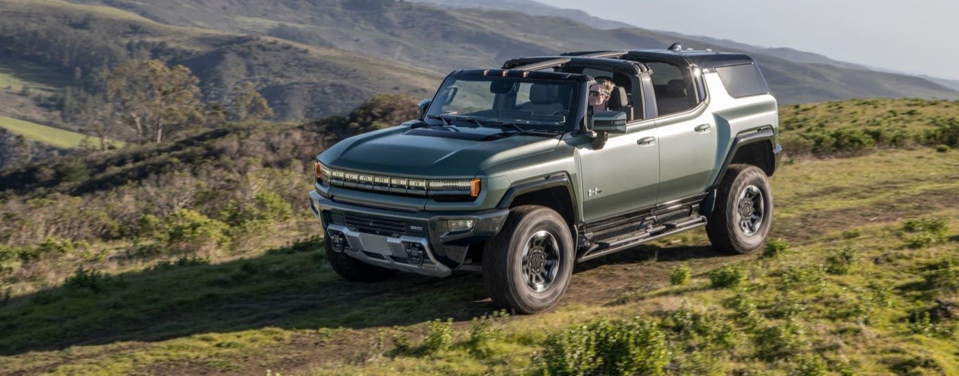 A green 2024 GMC Hummer EV driving on a trail.