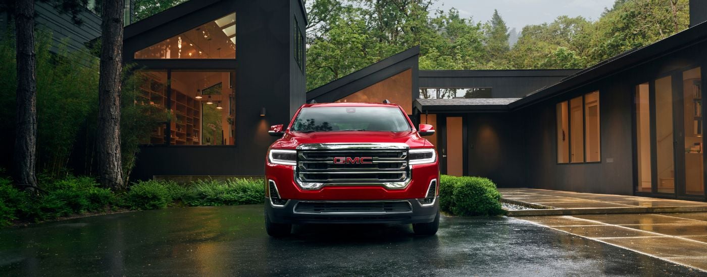 A red 2023 GMC Acadia parked outside a modern house.