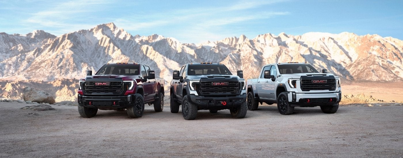 A red, a grey, and a white 2025 GMC Sierra 2500 for sale near Garland from the front.