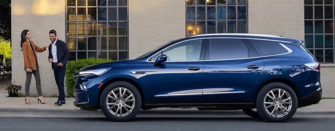 A blue 2023 Buick Enclave parked near two people.