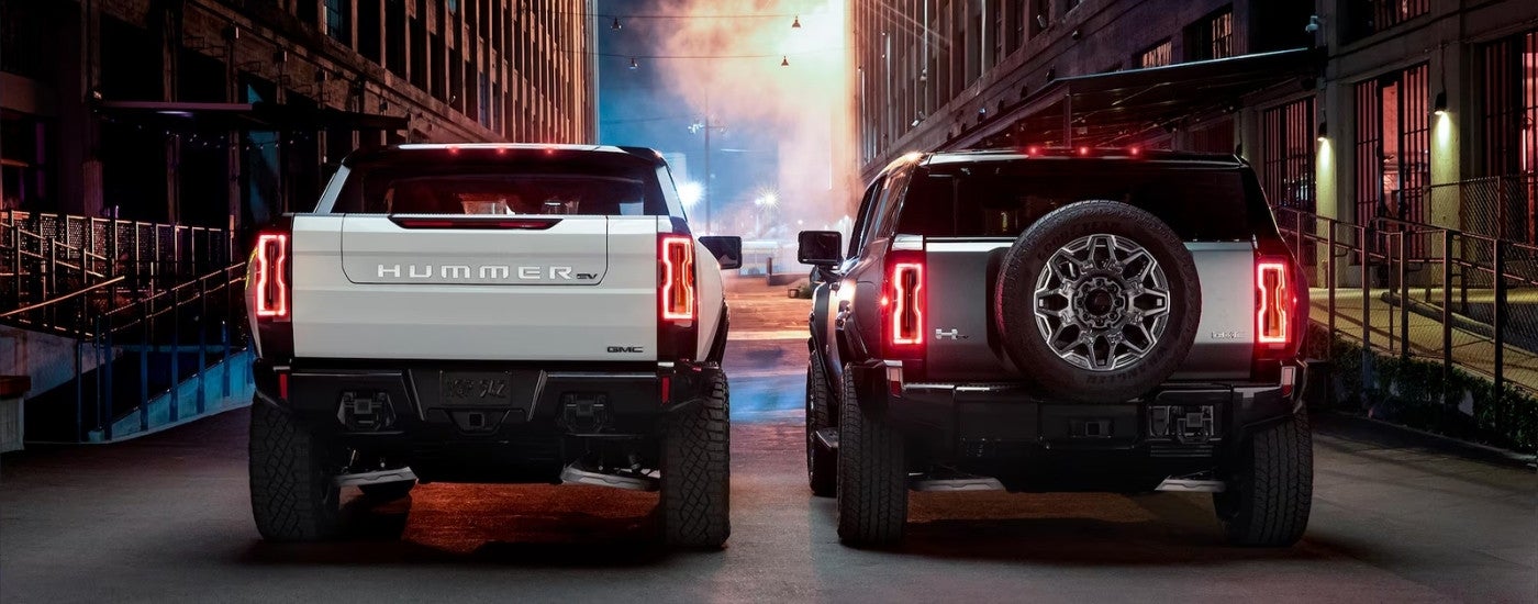 A white and a silver 2025 GMC Hummer EV are parked in a alleyway.