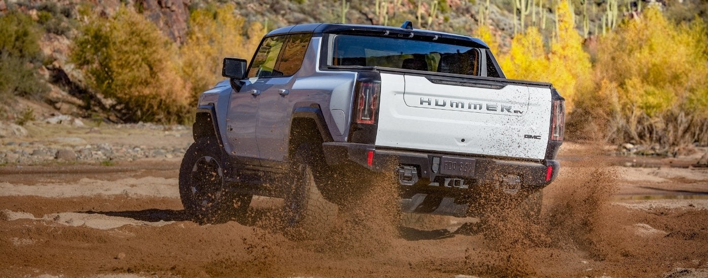 A white 2023 GMC Hummer EV is kicking up dirt off-road.